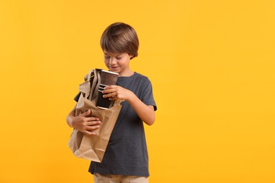 Photo of Recycling. Cute little boy with bag full of different waste paper on orange background, space for text