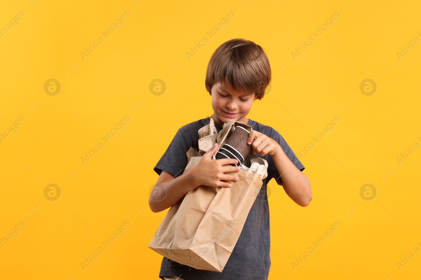 Photo of Recycling. Cute little boy with bag full of different waste paper on orange background