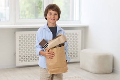 Photo of Recycling. Cute little boy with bag full of different waste paper at home