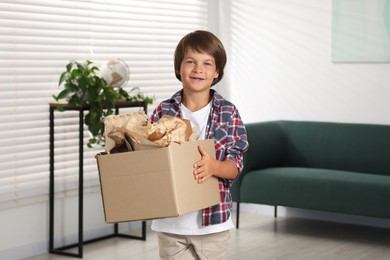 Photo of Recycling. Cute little boy with cardboard box full of different waste paper at home