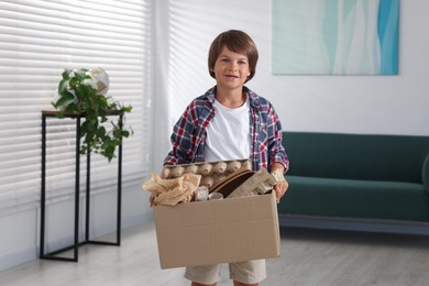 Photo of Recycling. Cute little boy with cardboard box full of different waste paper at home