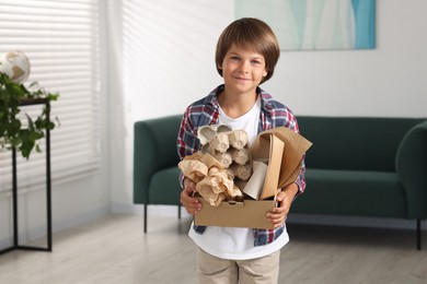 Photo of Recycling. Cute little boy with cardboard box full of different waste paper at home