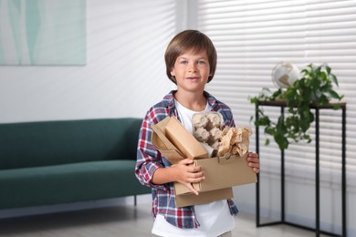 Photo of Recycling. Cute little boy with cardboard box full of different waste paper at home