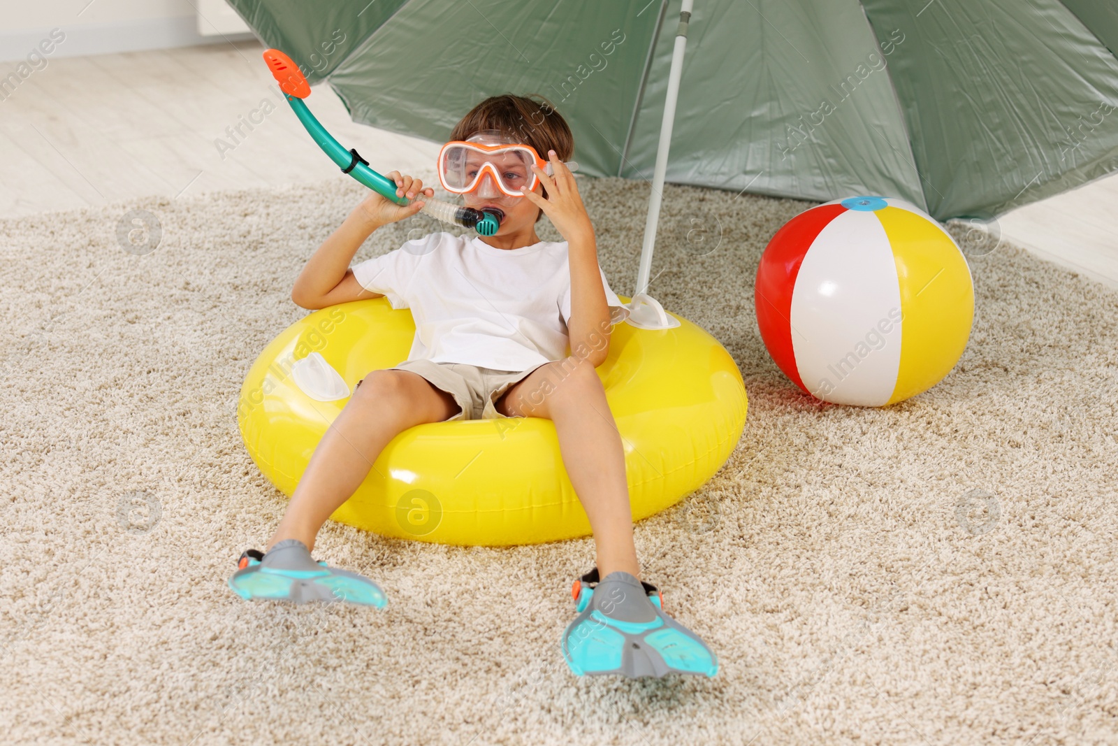 Dreaming about vacation at sea. Little boy with diving mask, snorkel, flippers and inflatable ring on floor indoors Photo of Dreaming about vacation at sea. Little boy with diving mask, snorkel, flippers and inflatable ring on floor indoors