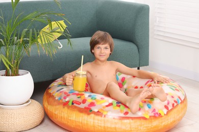 Photo of Dreaming about vacation at sea. Little boy with mason jar of fresh juice and inflatable ring on floor indoors