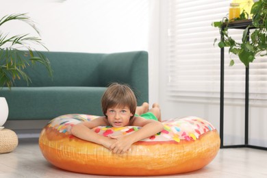 Photo of Dreaming about vacation at sea. Little boy on inflatable ring indoors