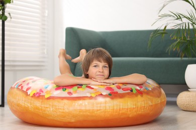 Photo of Dreaming about vacation at sea. Little boy on inflatable ring indoors