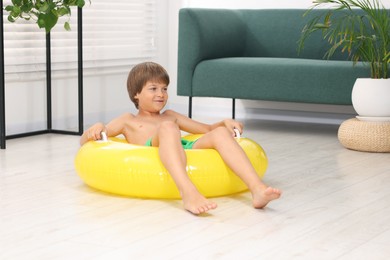 Photo of Dreaming about vacation at sea. Little boy with inflatable ring on floor indoors