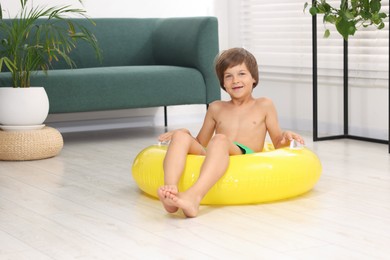 Photo of Dreaming about vacation at sea. Little boy with inflatable ring on floor indoors