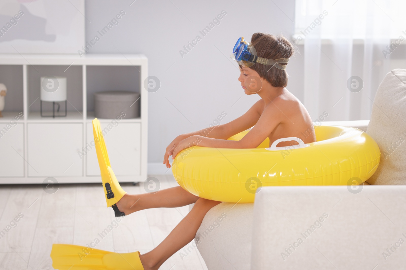 Dreaming about vacation at sea. Little boy with diving mask, flippers and inflatable ring in armchair indoors Photo of Dreaming about vacation at sea. Little boy with diving mask, flippers and inflatable ring in armchair indoors