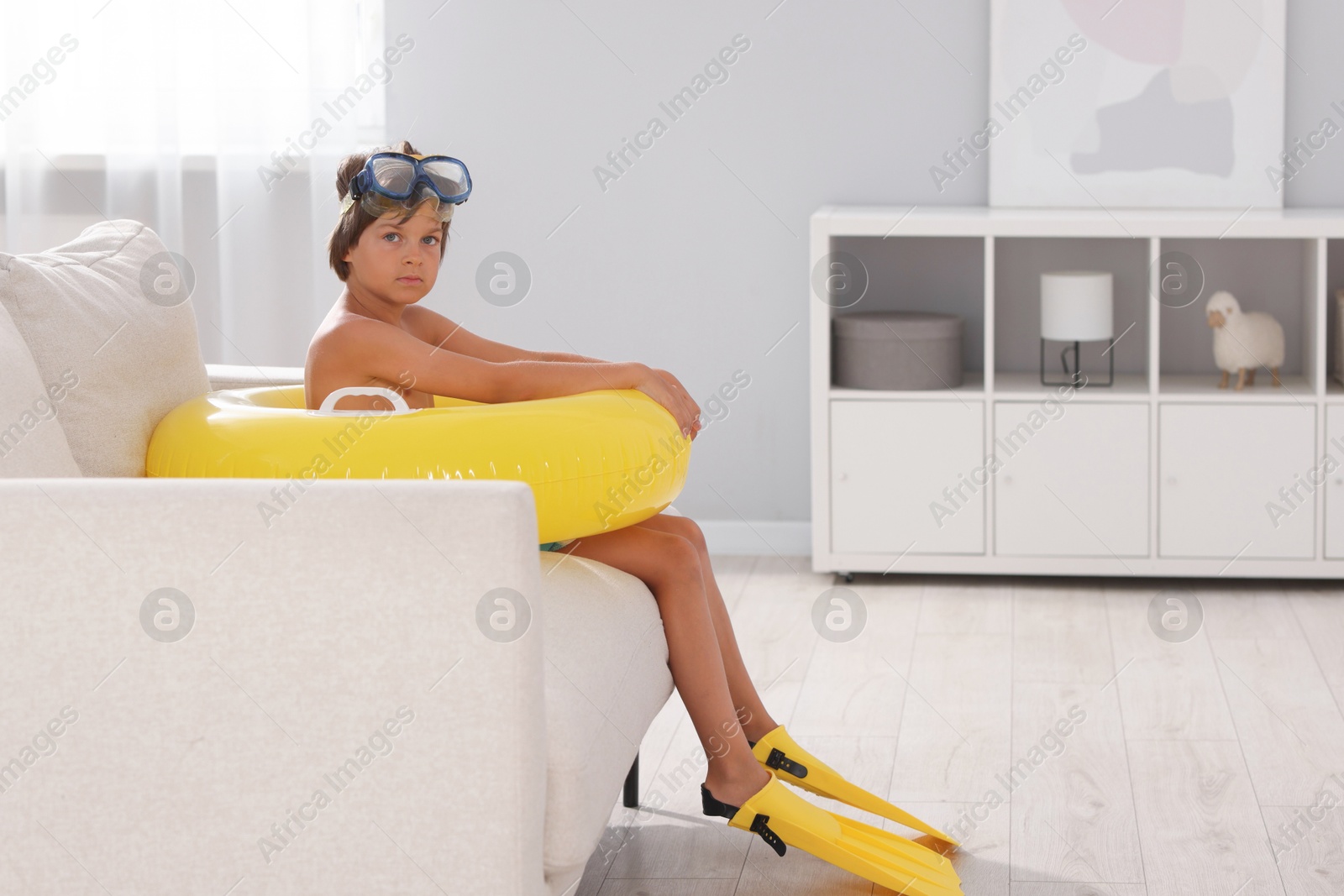 Photo of Dreaming about vacation at sea. Little boy with diving mask, flippers and inflatable ring in armchair indoors, space for text