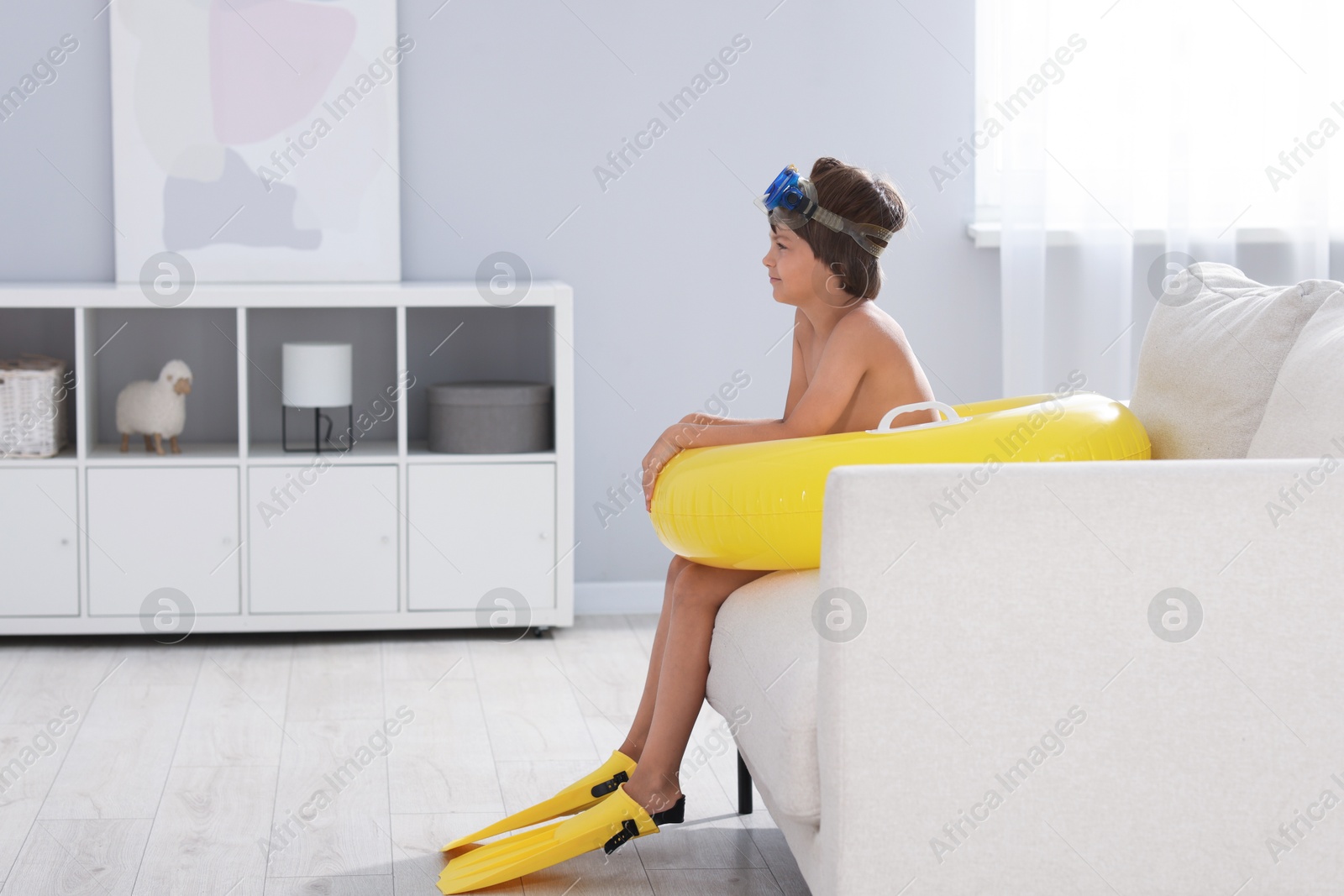 Dreaming about vacation at sea. Little boy with diving mask, flippers and inflatable ring in armchair indoors, space for text Photo of Dreaming about vacation at sea. Little boy with diving mask, flippers and inflatable ring in armchair indoors, space for text