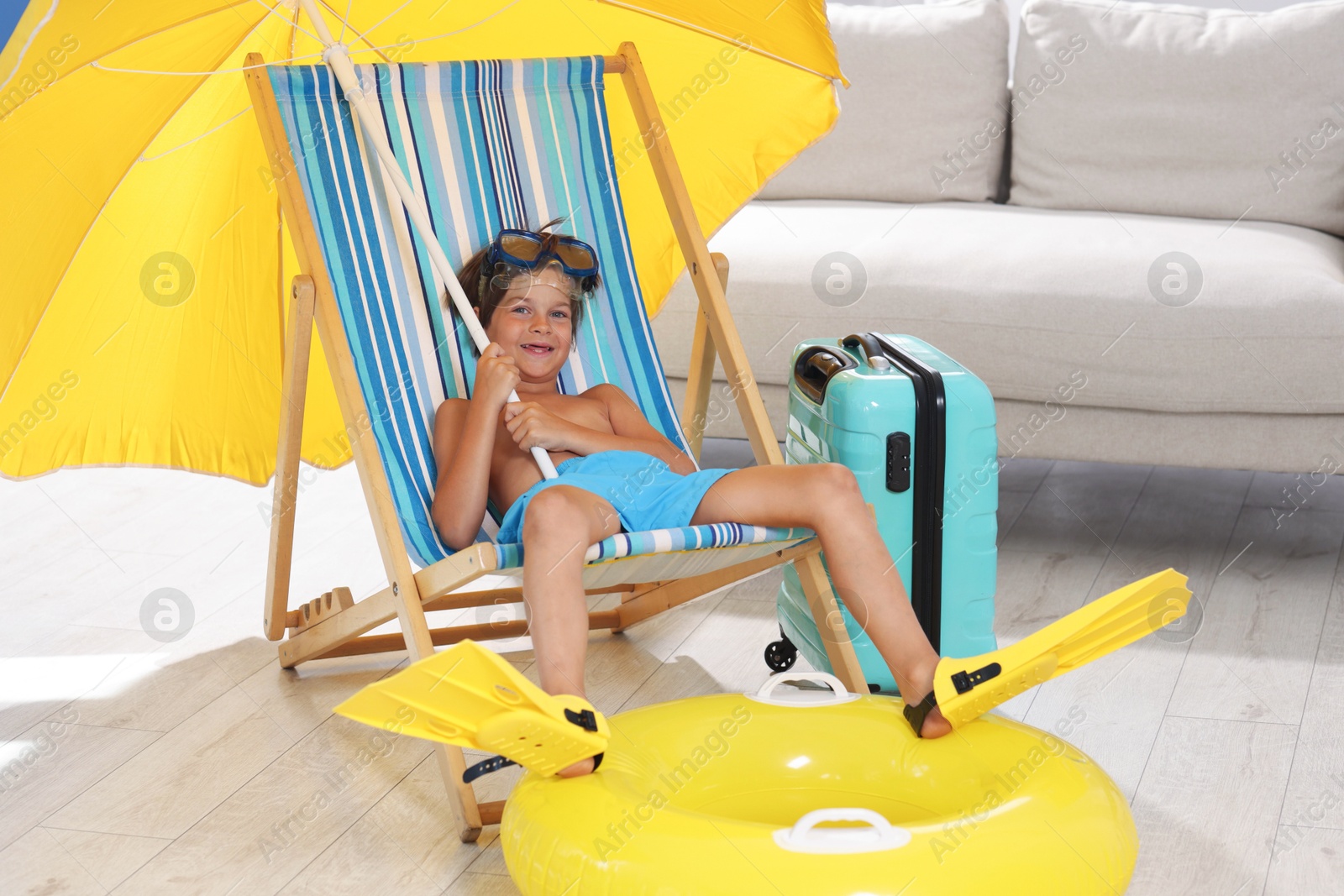 Dreaming about vacation at sea. Little boy with diving mask and flippers on deckchair near inflatable ring indoors Photo of Dreaming about vacation at sea. Little boy with diving mask and flippers on deckchair near inflatable ring indoors