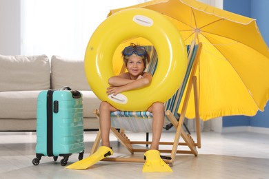 Photo of Dreaming about vacation at sea. Little boy with diving mask, flippers and inflatable ring on deckchair indoors