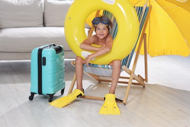 Photo of Dreaming about vacation at sea. Little boy with diving mask, flippers and inflatable ring on deckchair indoors