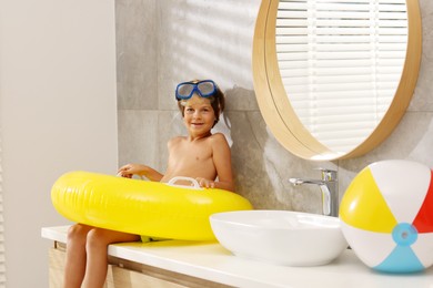 Photo of Dreaming about vacation at sea. Little boy with diving mask and inflatable ring in bathroom