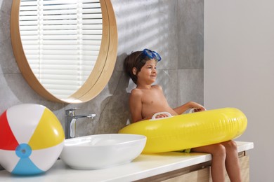 Photo of Dreaming about vacation at sea. Little boy with diving mask and inflatable ring in bathroom