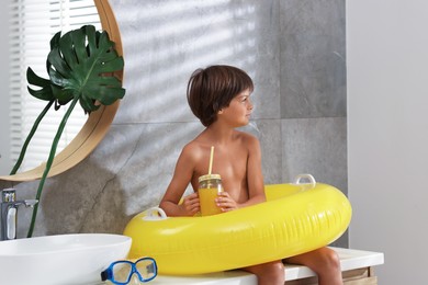 Photo of Dreaming about vacation at sea. Little boy with juice and inflatable ring in bathroom