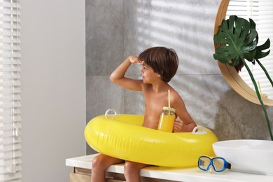 Photo of Dreaming about vacation at sea. Little boy with juice and inflatable ring in bathroom