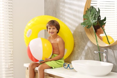 Photo of Dreaming about vacation at sea. Little boy with inflatable ring and ball in bathroom