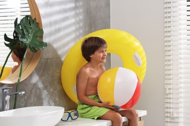 Photo of Dreaming about vacation at sea. Little boy with inflatable ring and ball in bathroom