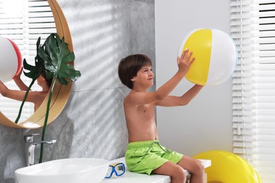 Photo of Dreaming about vacation at sea. Little boy with inflatable beach ball in bathroom