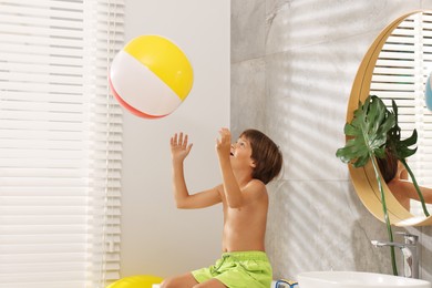 Photo of Dreaming about vacation at sea. Little boy with inflatable beach ball in bathroom