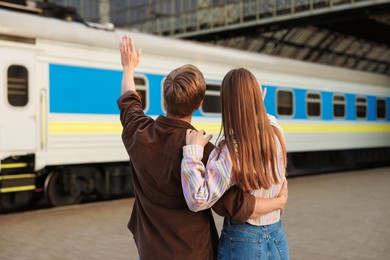 Photo of Goodbye. Couple waving on platform of railway station, back view
