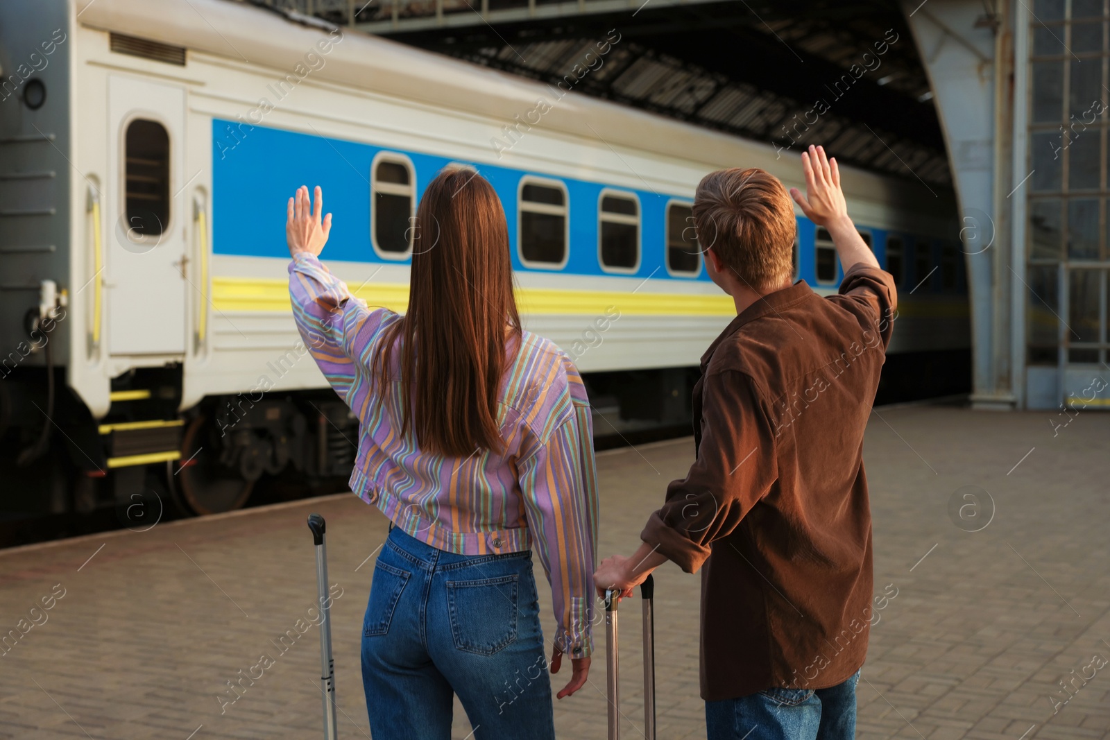 Goodbye. Couple with suitcases waving on platform of railway station, back view Photo of Goodbye. Couple with suitcases waving on platform of railway station, back view