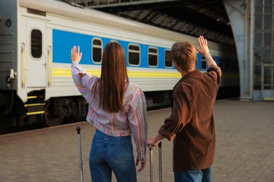 Photo of Goodbye. Couple with suitcases waving on platform of railway station, back view