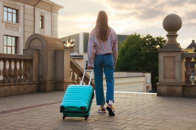 Photo of Goodbye. Woman with luggage walking on city street, back view