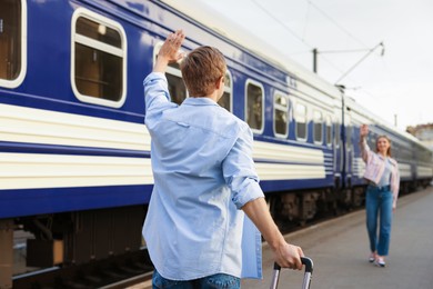 Photo of Goodbye. Man waving to his girlfriend near train outdoors, selective focus
