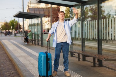 Photo of Goodbye. Man with luggage waving at bus stop
