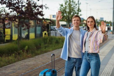 Photo of Goodbye. Lovely couple with suitcases waving at bus stop, space for text