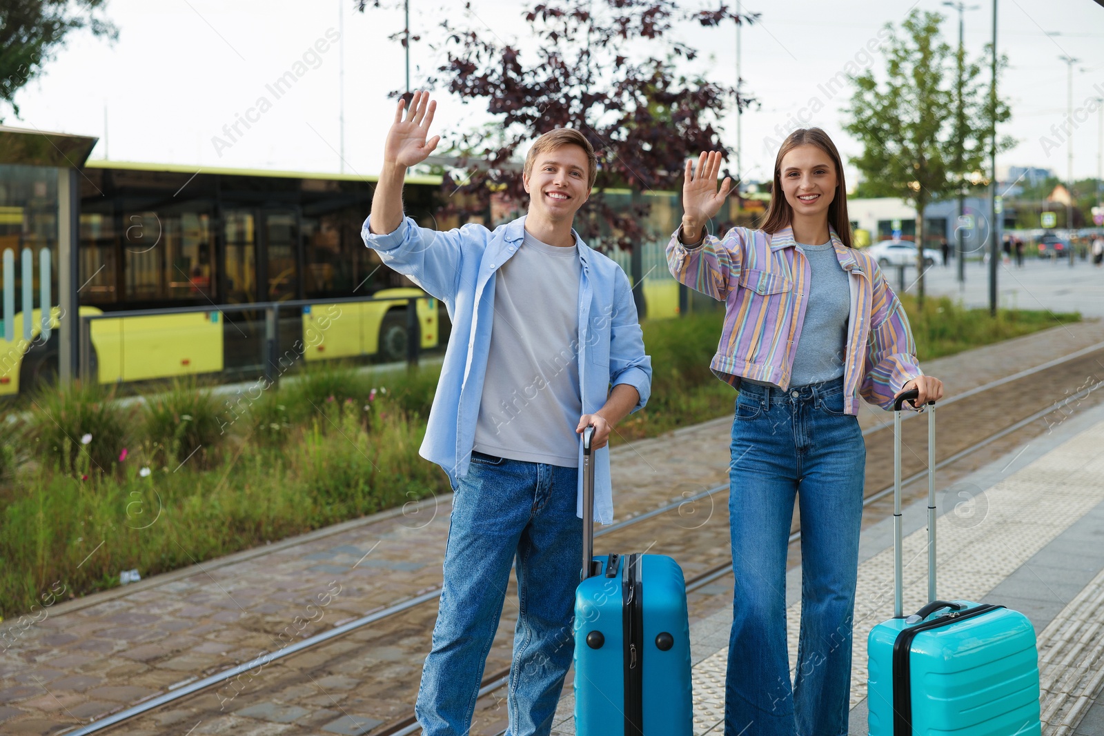Photo of Goodbye. Lovely couple with suitcases waving at bus stop, space for text