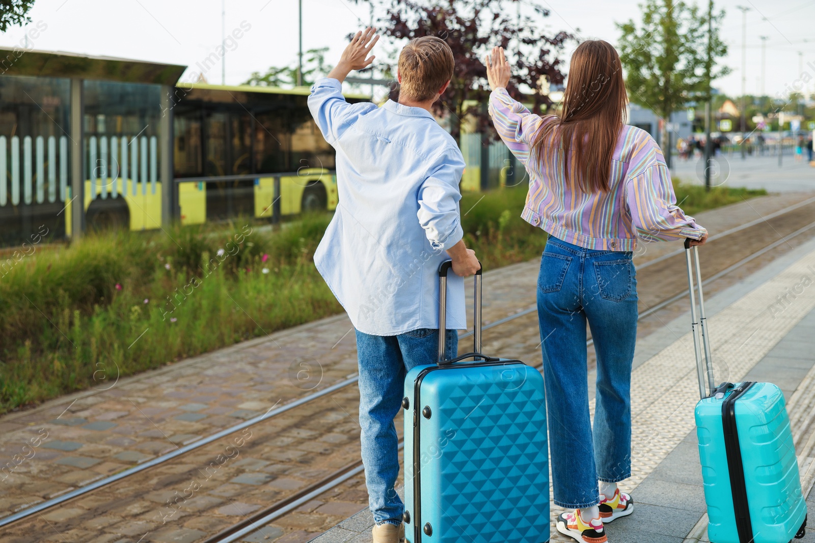 Goodbye. Couple with suitcases waving at bus stop, back view. Space for text Photo of Goodbye. Couple with suitcases waving at bus stop, back view. Space for text