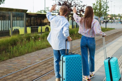 Photo of Goodbye. Couple with suitcases waving at bus stop, back view. Space for text