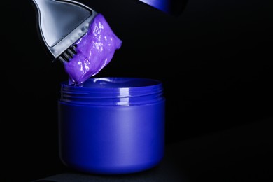 Photo of Brush with hair care cosmetic product for blonde hair over jar on black background, closeup. Space for text