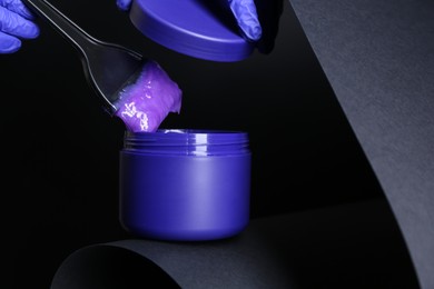 Photo of Woman taking hair care product for blonde hair with brush on black background, closeup