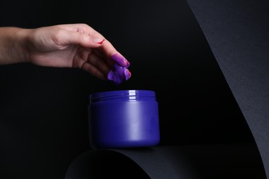 Photo of Woman taking hair care cosmetic product for blonde hair against black background, closeup. Space for text