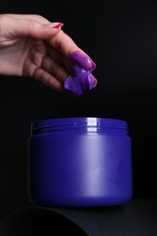 Photo of Woman taking hair care cosmetic product for blonde hair against black background, closeup