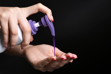 Photo of Woman using hair care cosmetic product for blonde hair on black background, closeup. Space for text