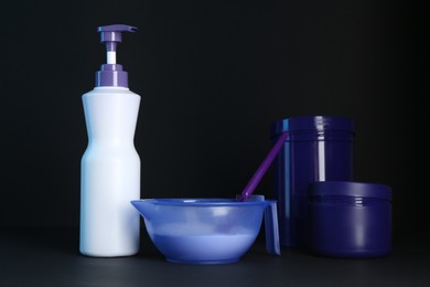 Photo of Different hair care cosmetic products for blonde hair and spatula on black background