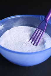 Photo of Blonde hair care cosmetic product. Powder in bowl and spatula on black background, closeup