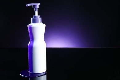 Photo of Bottle of hair care cosmetic products for blonde hair on black mirror surface against dark purple background, space for text