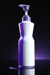 Photo of Bottle of hair care cosmetic products for blonde hair on black mirror surface against dark purple background