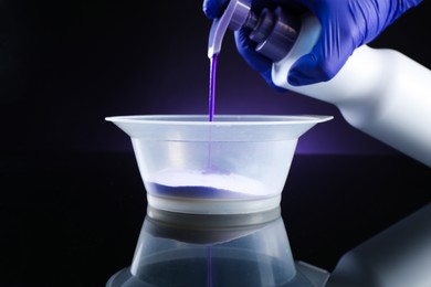 Photo of Woman making hair care product for blonde hair at black mirror table against dark purple background, closeup
