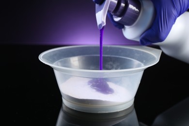 Photo of Woman making hair care product for blonde hair at black mirror table against dark purple background, closeup