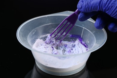 Photo of Woman making hair care product for blonde hair at black mirror table, closeup