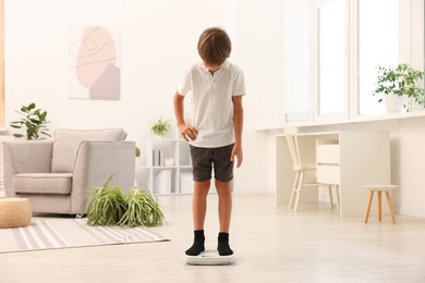 Photo of Little boy standing on scales at home